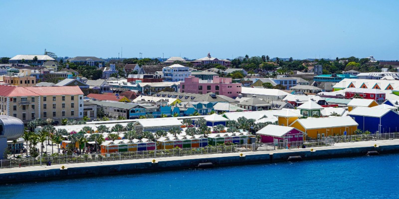 Waterfront view of a colorful coastal town with bright buildings, palm trees, and blue water in the foreground.